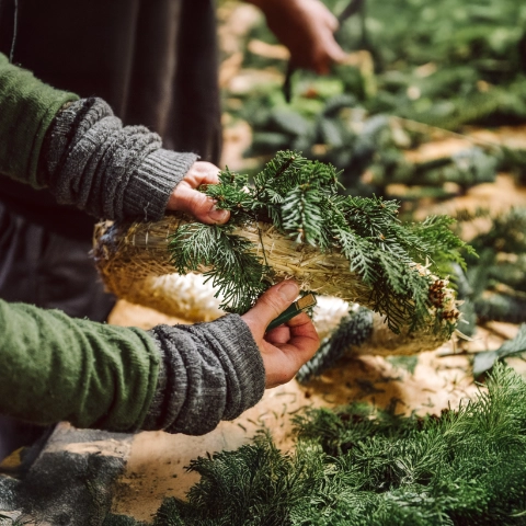 Hände, die einen Adventskranz aus Tannenzweigen binden.