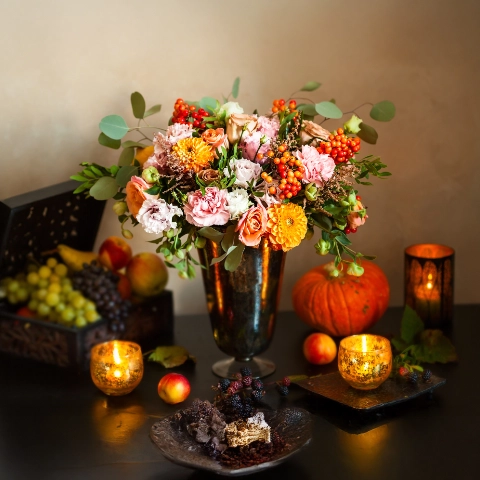 Herbstliches Stillleben mit opulentem Blumenstrauß, Kürbis, Trauben und Kerzen.